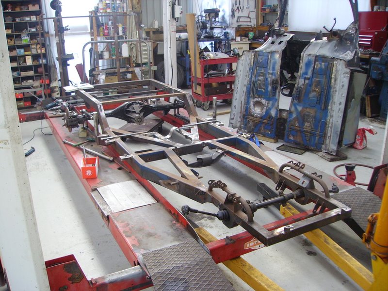Car chassis on a red lift in a workshop, with parts and tools in the background