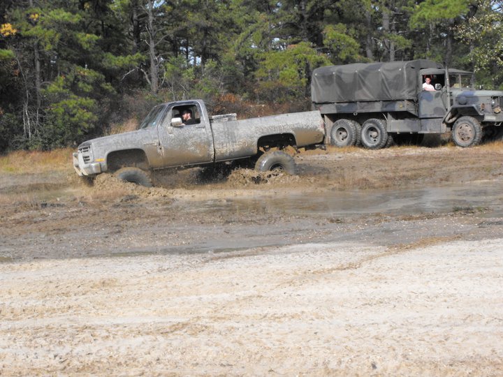 Muddy pickup truck stuck in a rut, being towed by a large military-style truck