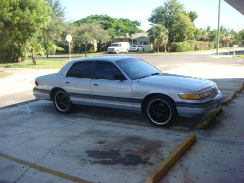 1994 Mercury Grand Marquis - A silver sedan with aftermarket black wheels is parked in a lot.