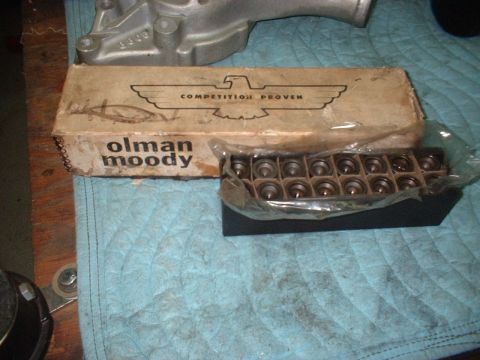 1964 Ford Galaxie - A box labeled 'olman moody' with an eagle logo sits next to a tray of engine parts and a metal pump.