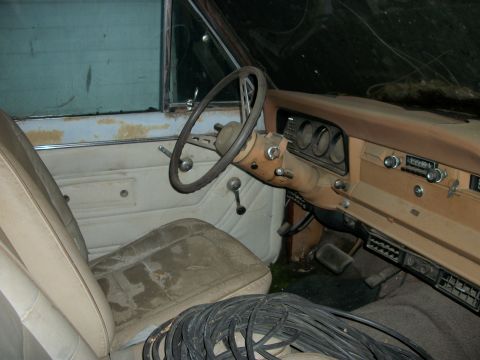 1976 Jeep J-10 - The interior of a 1976 Jeep J-10 shows significant wear and dust, with a tan dashboard and steering wheel.