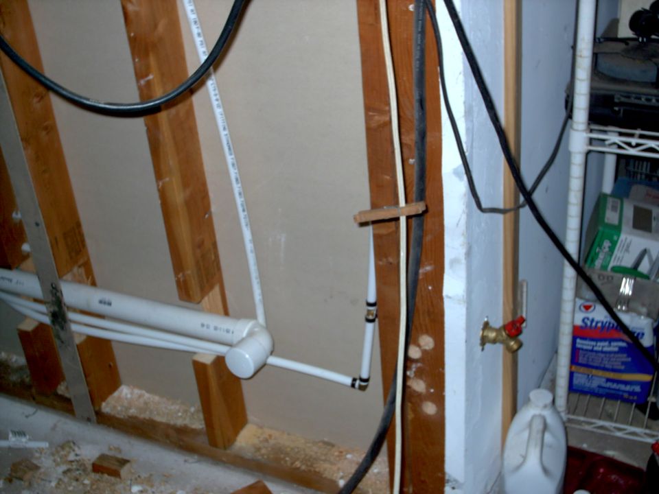 Exposed wall studs with PVC pipes, electrical wires, and a water spigot