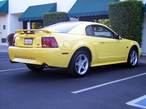 2002 Ford Mustang - A yellow 2002 Ford Mustang GT is parked in a lot, viewed from the rear-left quarter.