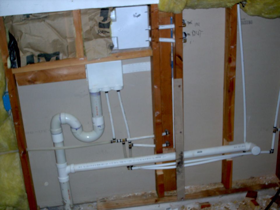 Plumbing pipes in wall cavity, some insulation visible. Text on wall says 'IN' and 'OUT'