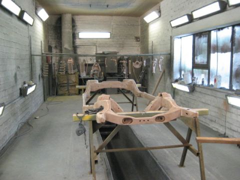1973 Ford Ranchero - Car frame assembly on sawhorses in a workshop with overhead lights and tools in background.