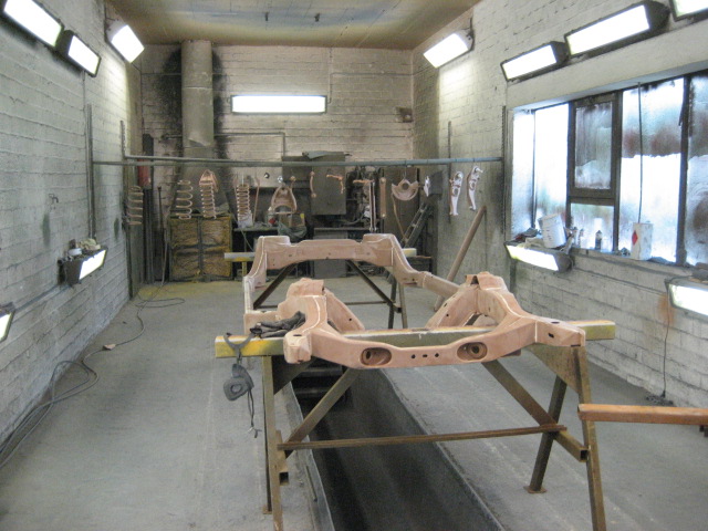 Car frame assembly on sawhorses in a workshop with overhead lights