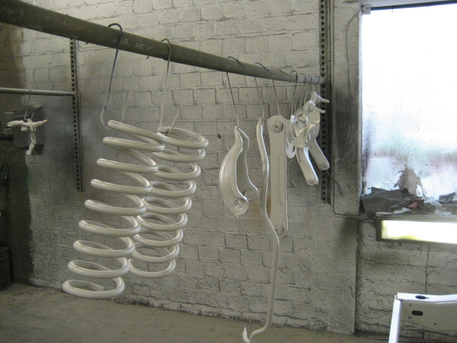 White painted suspension springs and linkage parts hanging from a metal rod in a workshop