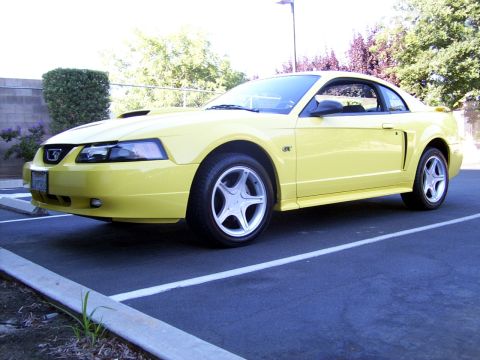 2002 Ford Mustang - A yellow 2002 Ford Mustang is parked in a lot, viewed from the front three-quarter angle.