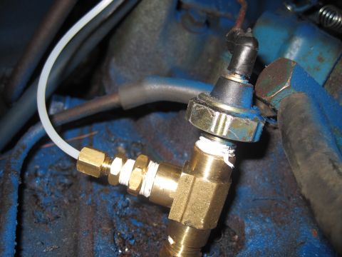 1979 Ford Bronco - Close-up of a brass fitting and sensor on a blue engine block.