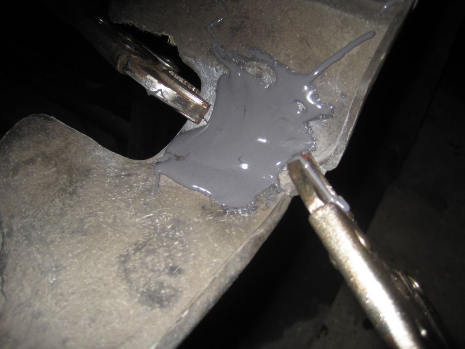 Close-up of a metal automotive part being repaired with grey putty and held by clamps