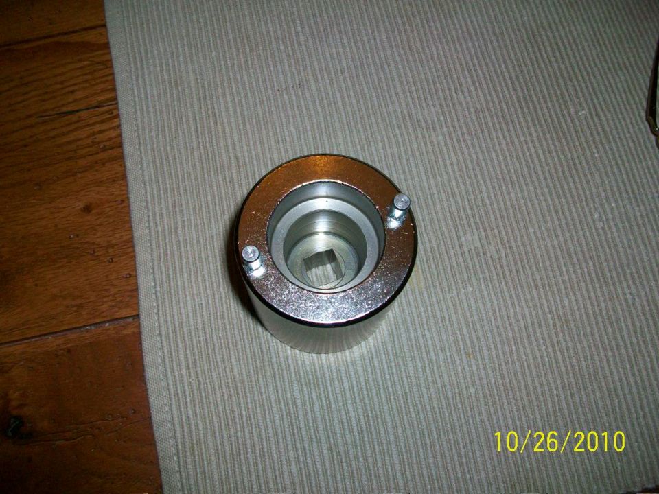 Chrome automotive tool with two small bolts on the outer rim and a square opening in the center
