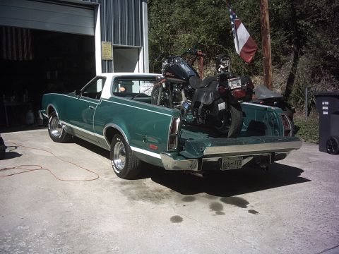 1996 Harley-Davidson Super Glide - A green El Camino is parked outside a garage with a motorcycle loaded in its bed. The vehicle's license plate is visible.