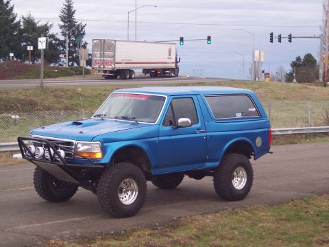 1984 Ford Bronco - This modified blue Ford Bronco is seen from a 3/4 front angle on a paved road.