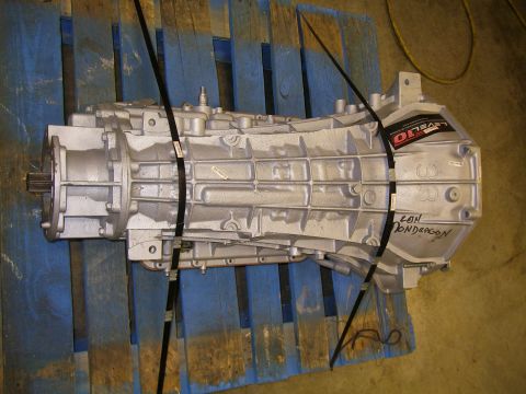 1990 Ford Bronco - A silver transmission casing is secured with black straps on a wooden pallet.