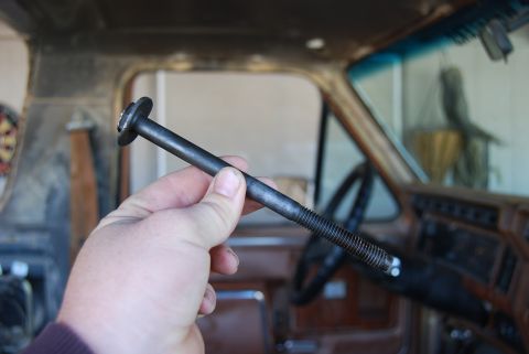 1982 Ford Bronco - A person holds a long bolt in the interior of a vehicle, with the dashboard and steering wheel visible.