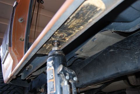 1982 Ford Bronco - A hydraulic jack is used to lift the frame of an orange vehicle.