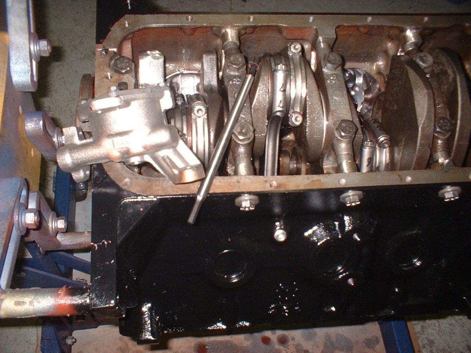 engine block with crankshaft, connecting rods, and oil pump assembly. A metal rod rests on the crankshaft