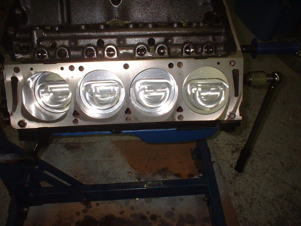 Engine block with four pistons visible, mounted on a stand