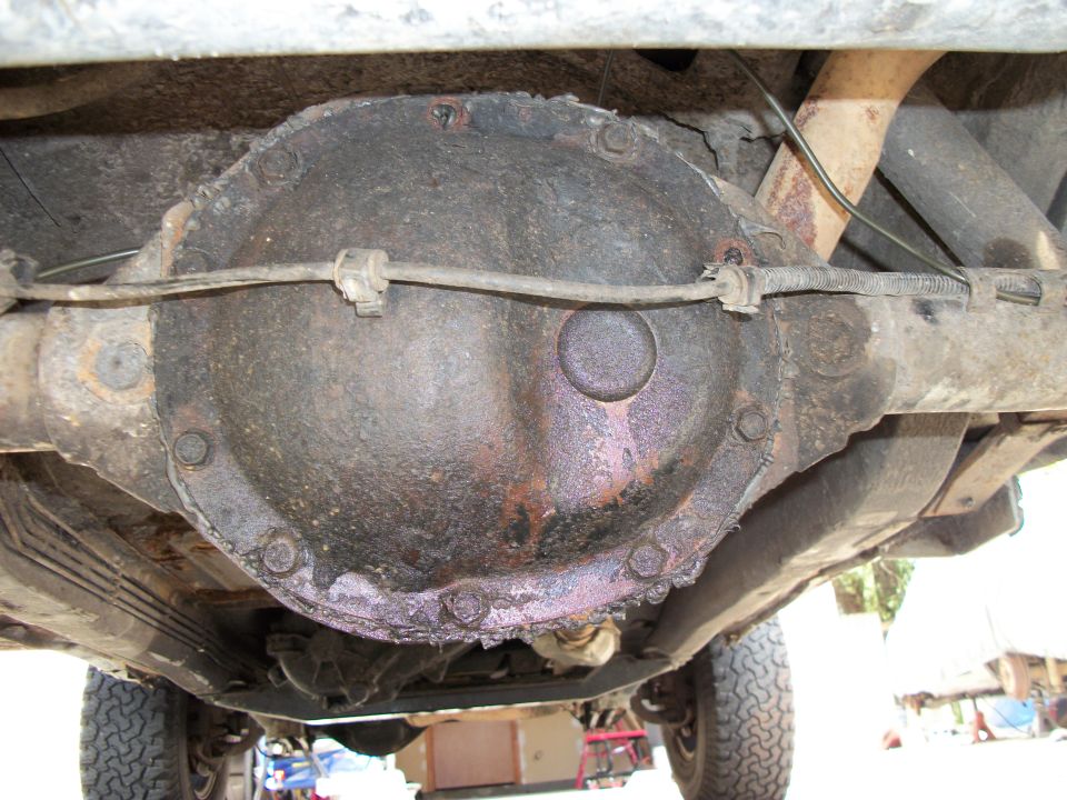 Underside of a vehicle showing a rusty rear differential with a brake line running across it