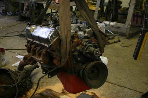 1973 Ford Ranchero - Engine assembly suspended by straps, showing its V8 configuration and chrome valve covers in a cluttered garage setting.
