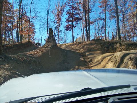 1987 Ford F-250 - A truck navigates a challenging dirt path through a wooded area with a clear blue sky above.