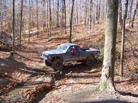 1987 Ford F-250 - A Jeep Comanche navigates a muddy trail through a forest during autumn.