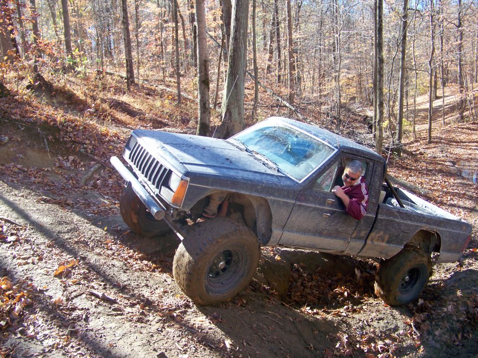 Dark gray Jeep Comanche pickup truck with large tires on a dirt trail