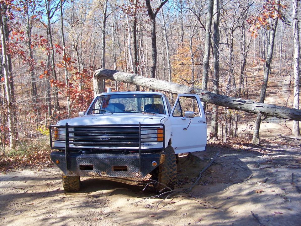 White 1987 Ford F-250 with open door, stuck on muddy trail
