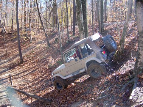 1987 Ford F-250 - A tan Jeep Wrangler navigates a steep, wooded trail during an off-road excursion.