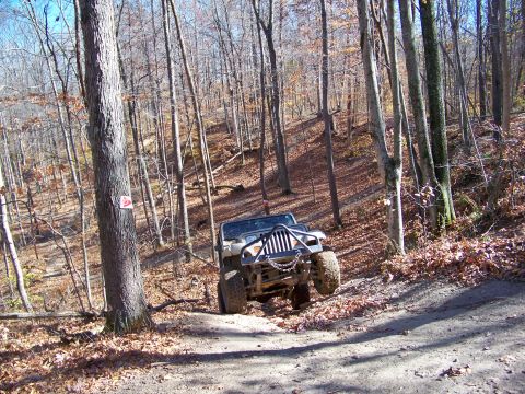 1987 Ford F-250 - A Jeep Wrangler navigates a steep, wooded trail during autumn.
