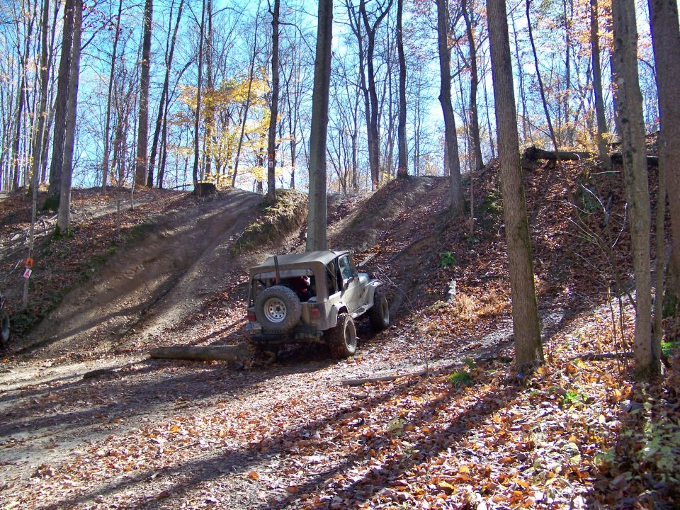 Tan off-road vehicle with spare tire on rear, on dirt path in woods