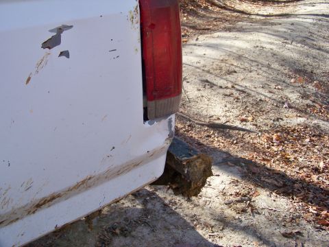 1987 Ford F-250 - The rear of a white pickup truck is shown with damage and mud, resting on a log.