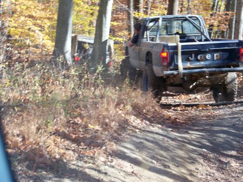 1987 Ford F-250 - Two off-road vehicles navigate a wooded trail during autumn.
