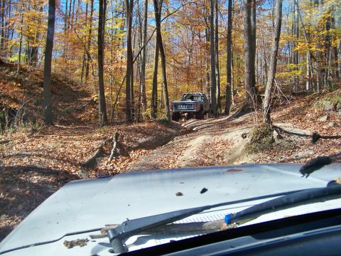 1987 Ford F-250 - A Jeep pickup truck navigates a wooded trail during fall foliage season.