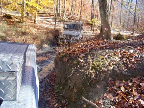 1987 Ford F-250 - Two vehicles traverse a muddy, leaf-strewn trail during an autumn off-road excursion.