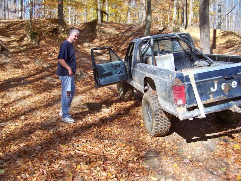 1987 Ford F-250 - Man stands next to a modified Jeep Comanche pickup truck on an off-road trail during autumn.