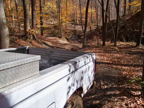 1987 Ford F-250 - A white 1987 Ford F-250 pickup truck navigates a wooded trail during autumn.