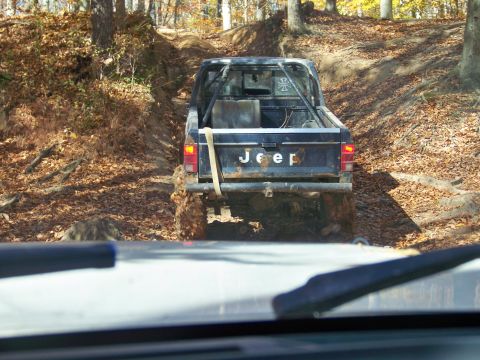 1987 Ford F-250 - Jeep pickup truck navigates a muddy, wooded trail during an off-road excursion.