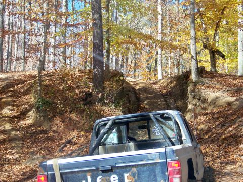 1987 Ford F-250 - A Jeep pickup truck navigates a muddy off-road trail surrounded by fall foliage.