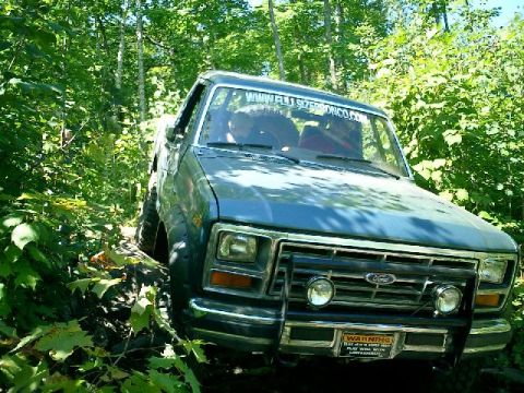 1986 Ford Bronco - This blue Ford Bronco navigates a wooded trail, its grille and front bumper clearly visible.
