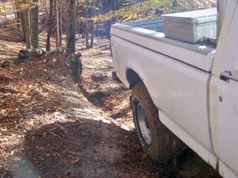 1987 Ford F-250 - A white 1987 Ford F-250 navigates a muddy, wooded trail during an off-road excursion.