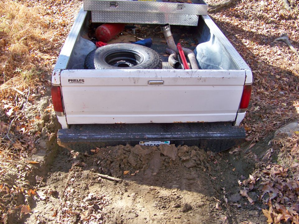 White pickup truck rear stuck in mud, spare tire and toolbox in bed