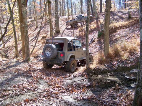 1987 Ford F-250 - Two off-road vehicles navigate a muddy, leaf-covered trail through a forest in autumn.