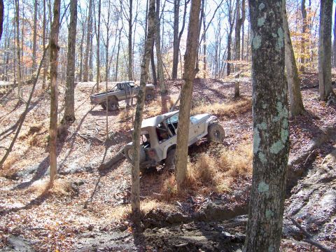1987 Ford F-250 - Two off-road vehicles are seen on a trail in a wooded area during the fall.