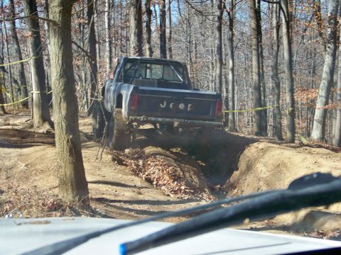 1987 Ford F-250 - A Jeep Comanche navigates a challenging off-road course in a wooded area.