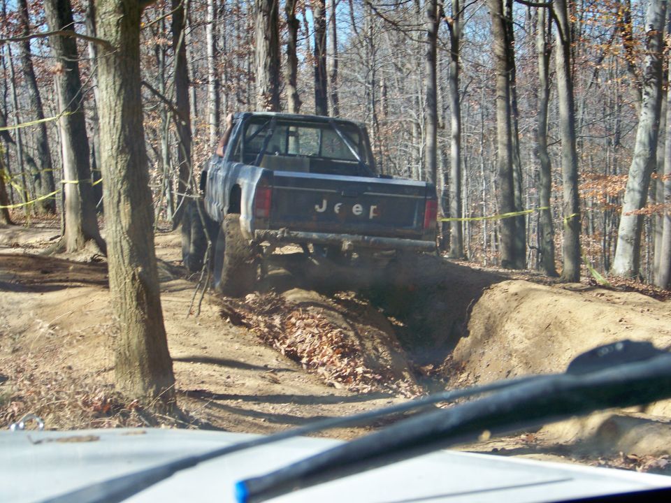 Jeep Comanche pickup truck driving on a dirt trail in woods