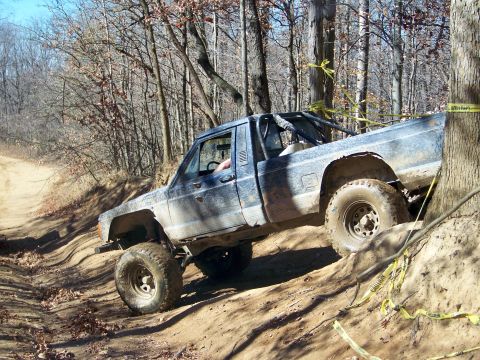 1987 Ford F-250 - A blue pickup truck navigates a steep, wooded trail during an off-road excursion.