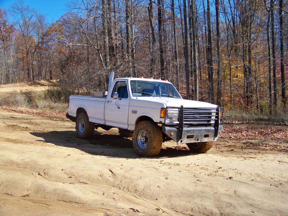 White 1987 Ford F-250 pickup truck with tall exhaust pipe on a dirt road