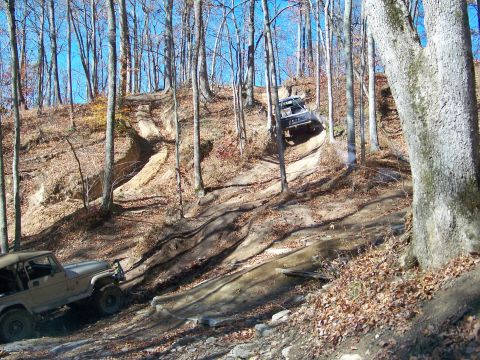 1987 Ford F-250 - Off-road vehicles ascend a challenging dirt path through a forest during autumn.