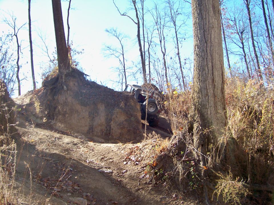 Off-road vehicle climbing a steep, muddy hill next to a large tree